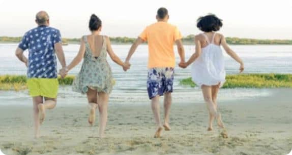 Quatre personnes (deux couples) se tenant par la main courant ensemble sur le sable vers le bord de mer