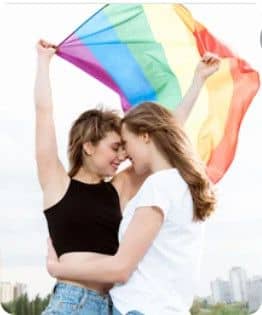 Deux femmes s'enlaçant, l'une tenant tout haut un drapeau couleur arc-en-ciel