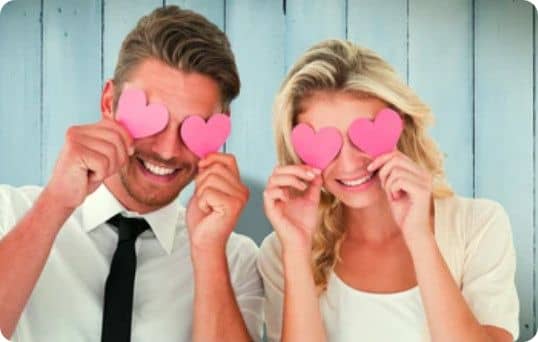 Couple se cachant les yeux avec des coeurs en papier rose