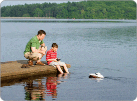 P+¿re et enfant au bord d'un lac télécommandant un petit bateau
