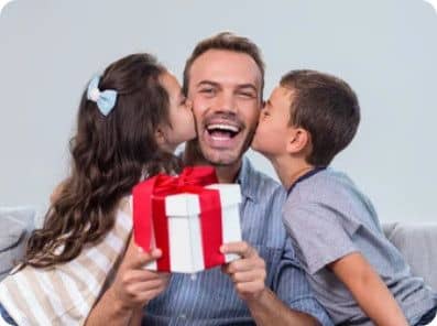 Papa souriant tenant un cadeau, recevant les bisous de ses deux enfants