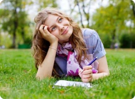 Femme couchée sur les herbes, stylo à la main, regardant le ciel pour chercher son inspiration